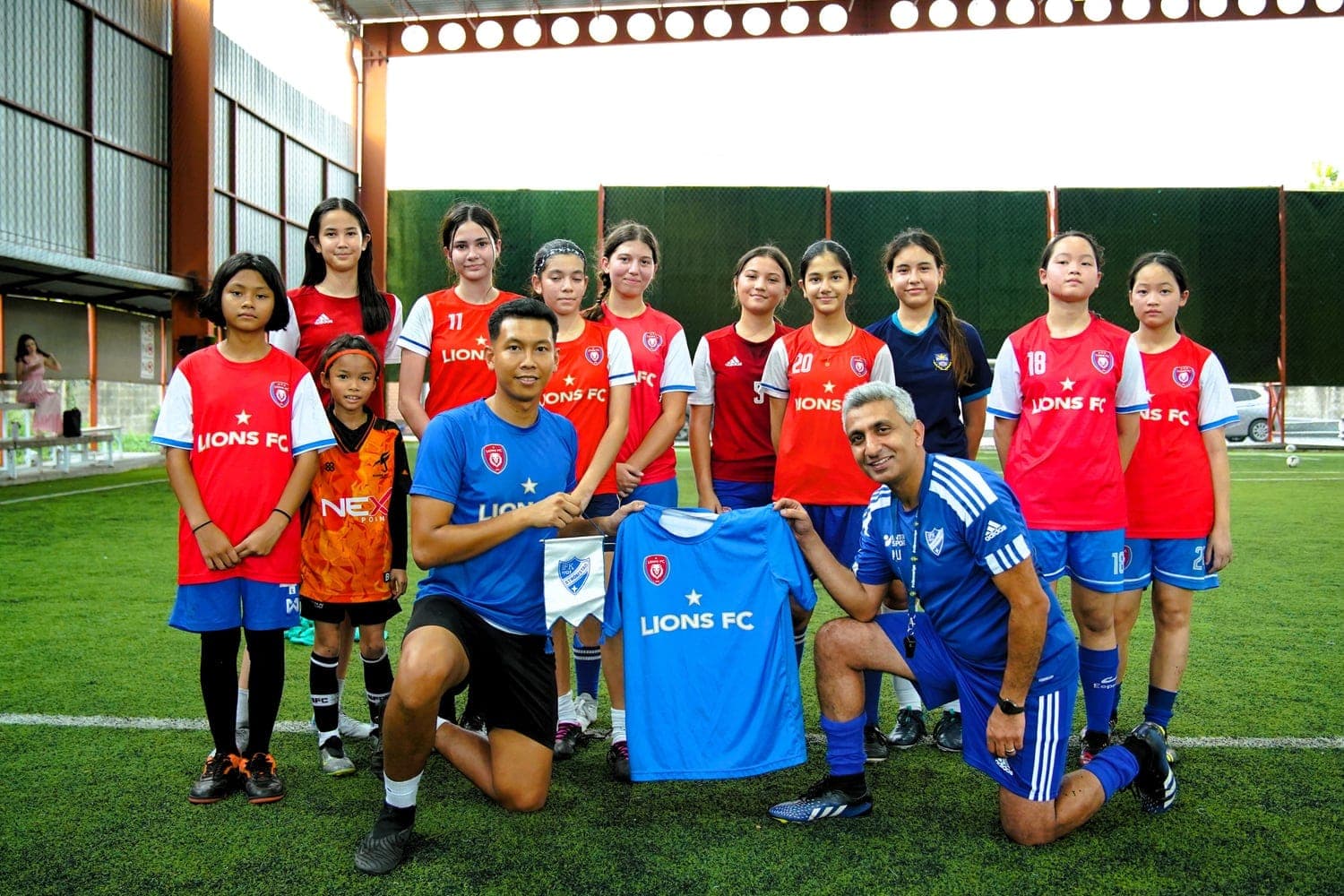 The squad with their coaches and a visiting coach, holding a club shirt between them