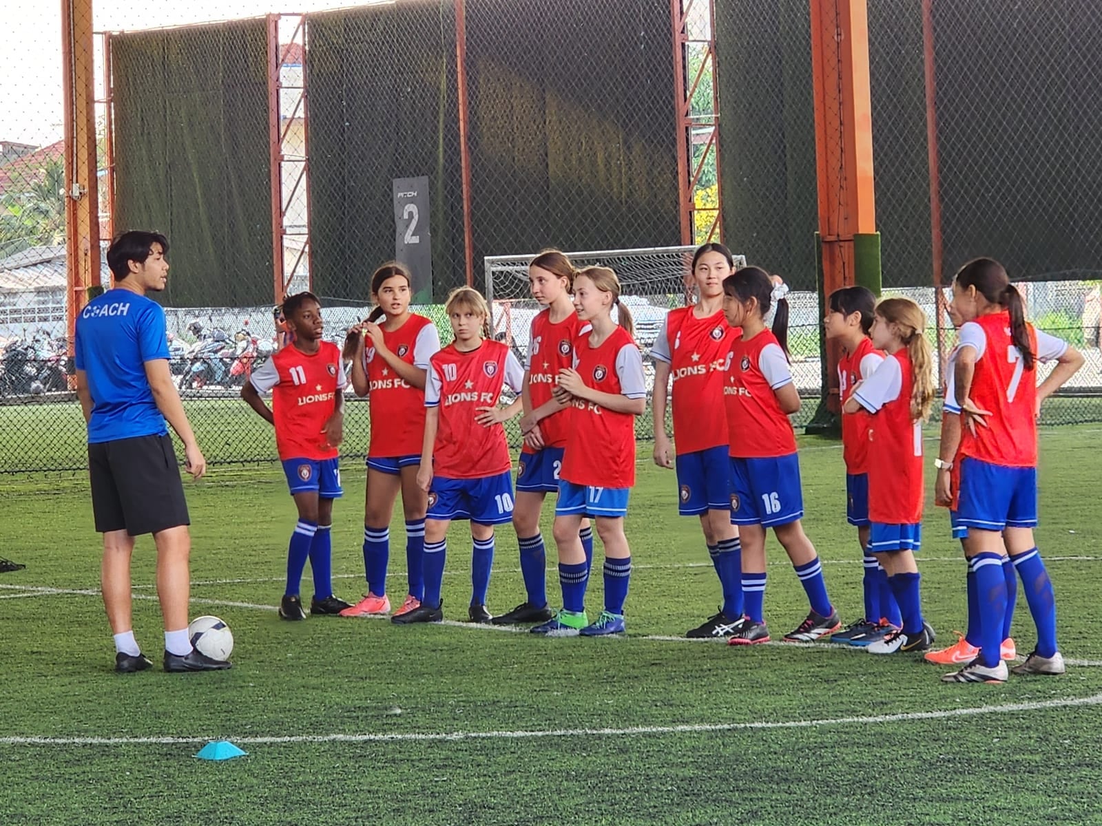 The Lions FC squad gathered around their coach on the covered pitch at SoccerPro Bangna before a training session